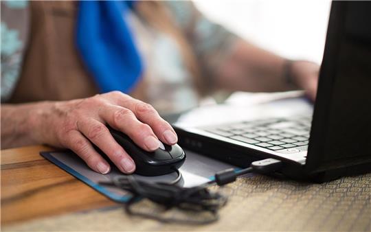 Eine Seniorin sitzt an ihrem Laptop.