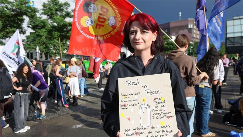 Eine Sozialarbeiterin hält ein Pappschild. Darauf steht etwa „Rest in Peace“ und „Sozialarbeiter*innen trauern um Sozialarbeiter*innen“.