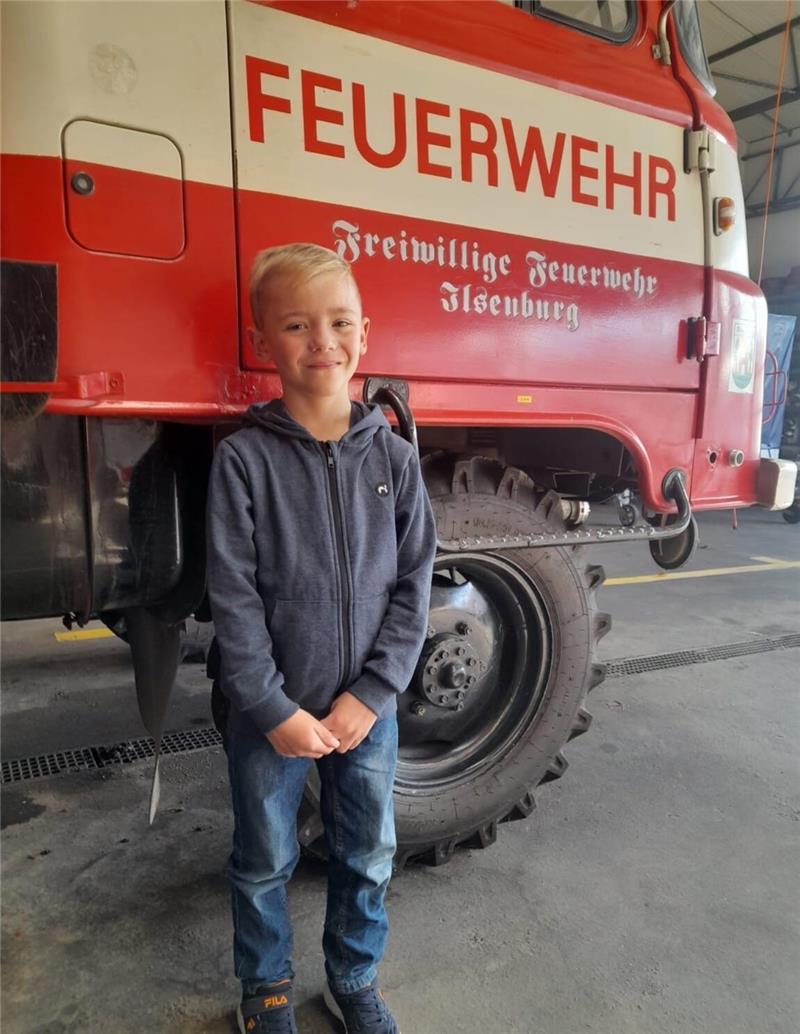 Ein neunjähriger Junge steht vor einem Feuerwehrauto.