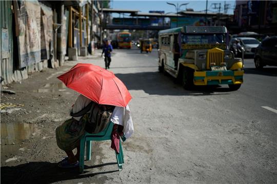 Eine Straßenverkäuferin schützt sich in Manila mit einem Regenschirm vor der Sonne.
