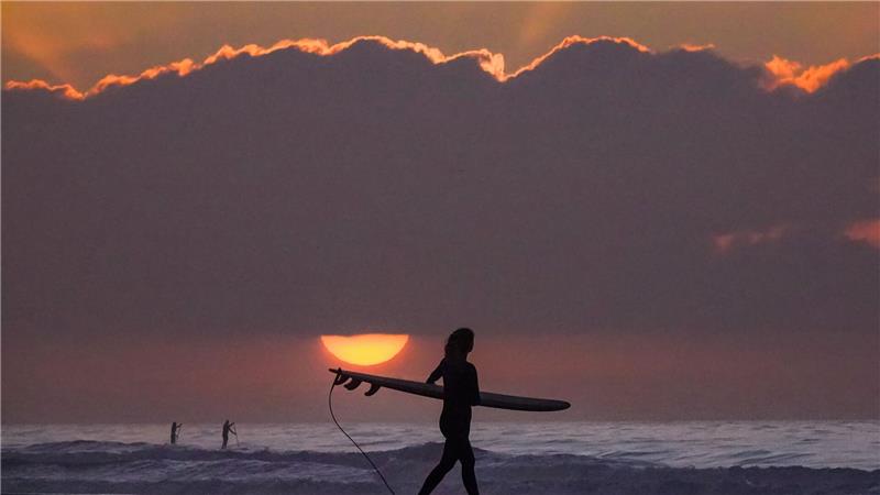 Eine Surferin trägt ihr Surfbrett in Richtung Meer.