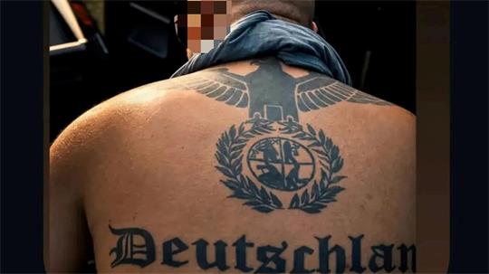 Rückenansicht eines Mannes mit großem schwarzen Tattoo eines Adlers über einem Lorbeerkranz mit einem runden Symbol in der Mitte.