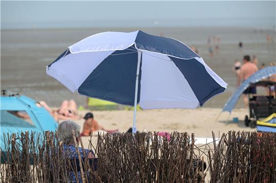 Eine ältere Frau sitzt sommerlichem am Badestrand unter ihrem Sonnenschirm.