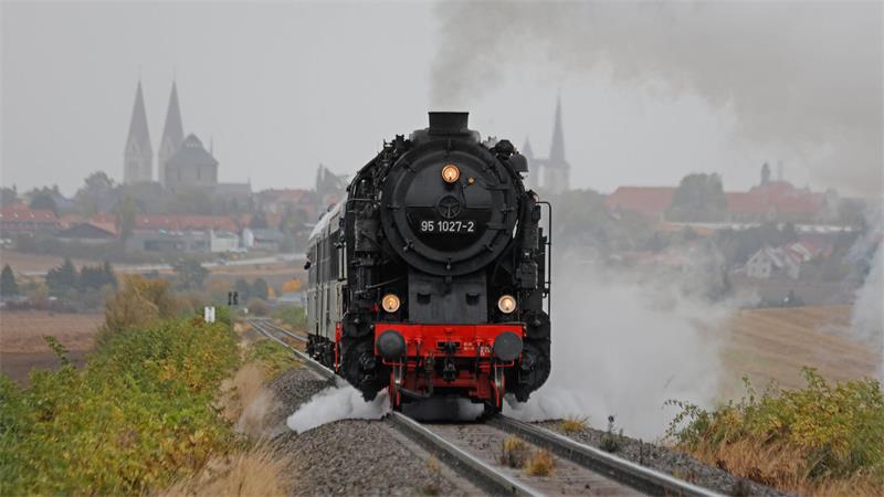 Eine Dampflok fährt auf den Schienen. Im Hintergrund ist Magdeburg mit seinen Kirchen zu sehen.