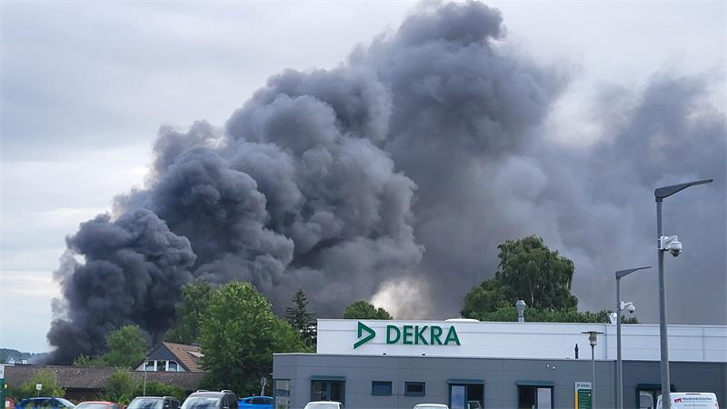 Dichter schwarzer Rauch steigt hinter einem Gebäude mit dem Schriftzug 'DEKRA' auf