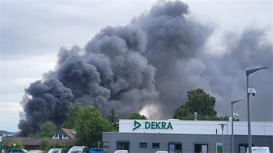 Dichter schwarzer Rauch steigt hinter einem Gebäude mit dem Schriftzug 'DEKRA' auf