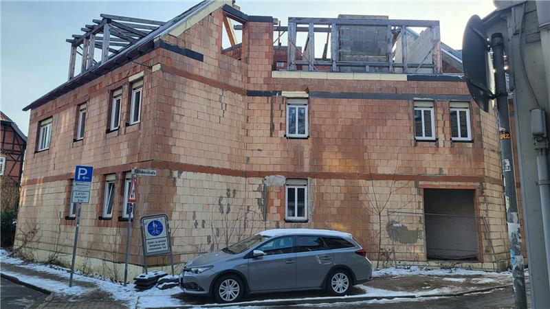 Unfertiges zweistöckiges Backsteingebäude mit mehreren Fenstern und einem geparkten Auto davor