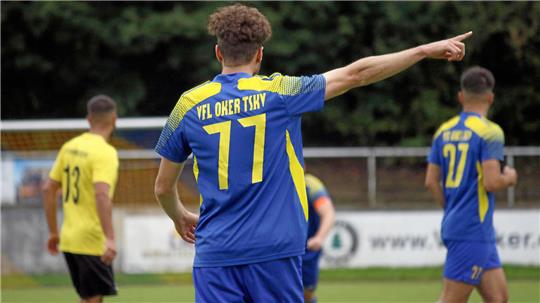 Fußballspieler mit blau-gelbem Trikot und der Nummer 77 zeigt mit ausgestrecktem Arm nach rechts, weitere Spieler im Hintergrund auf dem Spielfeld