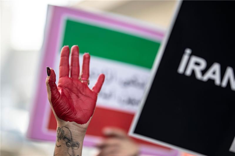 Eine rot bemalte Hand einer Frau erhebt sich zwischen Plakaten während einer Demonstration.
