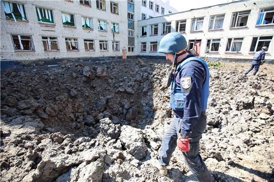 Eine ukraininische Sicherheitskraft inspiziert das Gelände einer Schule in Charkiw nach russischem Beschuss.