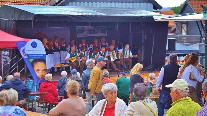 Eine Brauchtumsgruppe musiziert auf einer Bühne vor Menschen.