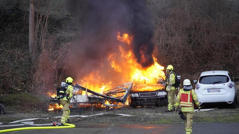 Ein brennendes Auto, das von Feuerwehrleuten gelöscht wird.