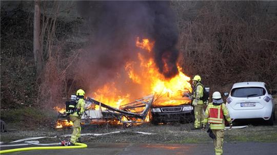 Ein brennendes Auto, das von Feuerwehrleuten gelöscht wird.