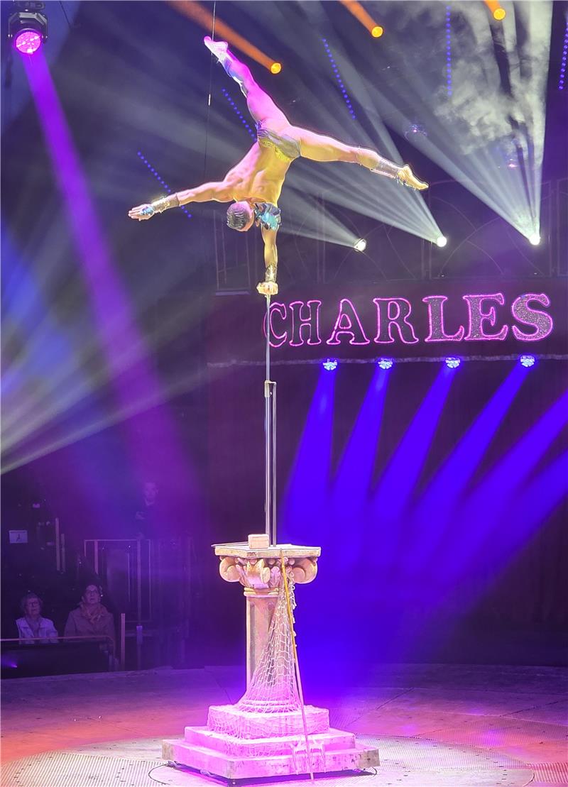 Osterfeld: Nach Neptuns Catwalk geht es zum Unterwasserball Akrobat in Goldkostüm balanciert kopfüber an einer Stange auf einer Säule mit Netz im Zirkus mit Bühnenbeleuchtung und Schriftzug 'CHARLES' im Hintergrund
