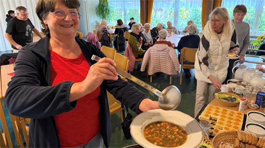 Das Foto zeigt eine Frau, die einen Teller mit Suppe füllt.