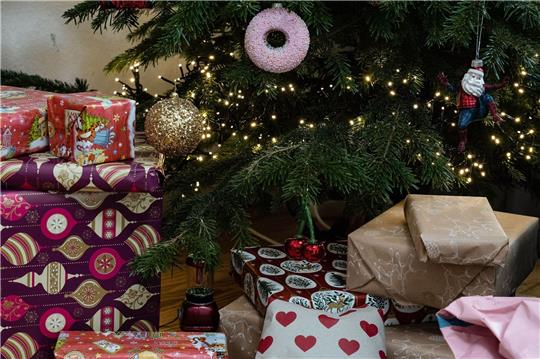 Eingepackte Geschenke liegen unter einem geschmückten Weihnachtsbaum. Die Menschen in Deutschland wollen in diesem Jahr bei den Geschenken sparsamer sein.