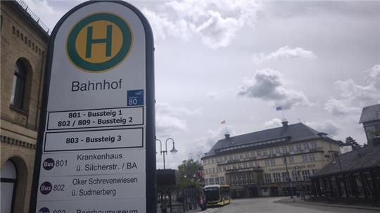 Haltestellenschild mit dem Schriftzug 'Bahnhof' und Buslinieninformationen vor einem historischen Bahnhofsgebäude und einer Straße mit wartendem Bus