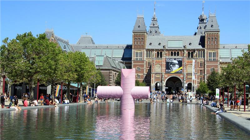 Der Haupteingang vom Rijksmuseum in Amsterdam, davor befindet sich ein Becken mit Wasser, an dem viele Menschen sitzen. 