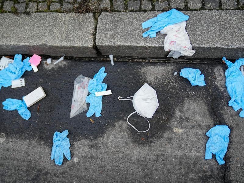 Einmalhandschuhe, FFP2-Maske und benutzte Corona-Antigen-Testkits liegen auf der Straße vor einem Corona-Testzentrum. Foto: Kay Nietfeld/dpa