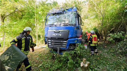 Einsatzkräfte der Feuerwehr stehen neben dem verunfallten Lkw an der Bundesstraße B3.