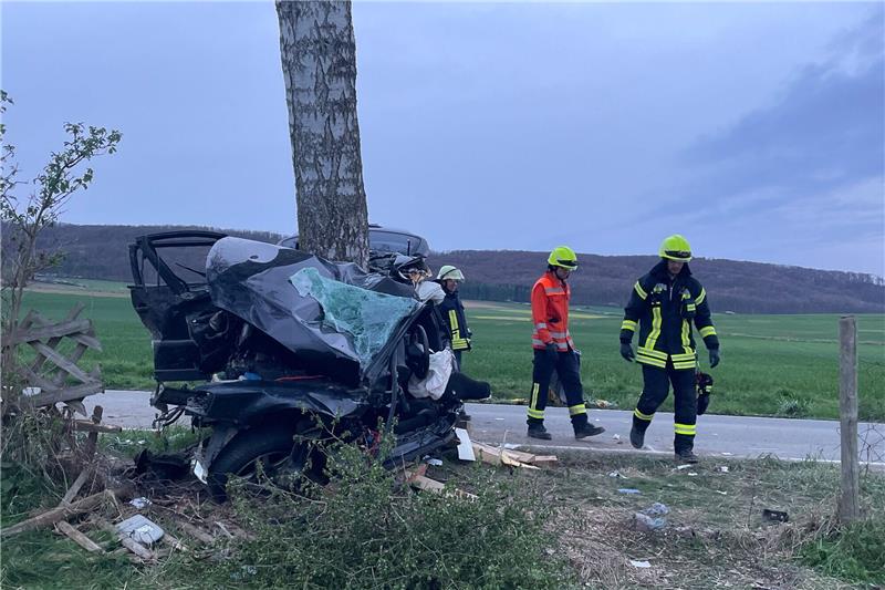 Einsatzkräfte der Feuerwehr stehen neben einem zerstörten Auto.