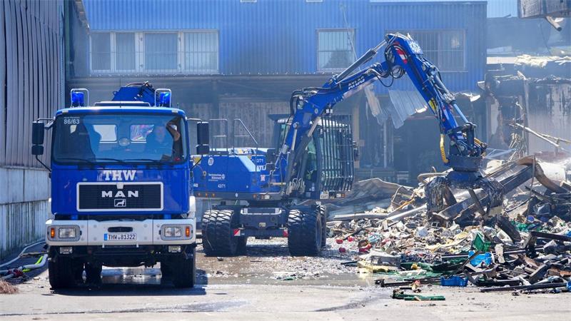 Einsatzkräfte des Technischen Hilfswerks (THW) beseitigen mit einem Bagger Schutt.