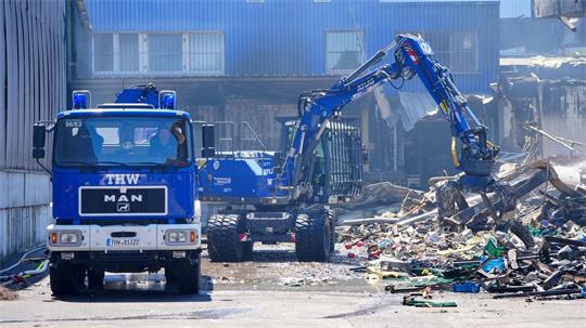 Einsatzkräfte des Technischen Hilfswerks (THW) beseitigen mit einem Bagger Schutt.