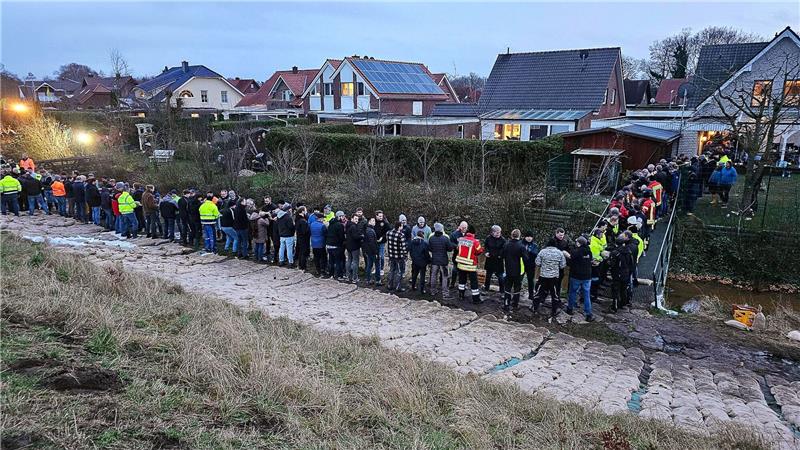 Beschädigungen an Deich im Emsland: Feuerwehr sichert Einsatzkräfte und Einwohner sichern gemeinsam einen durchweichten Deich in Haren.