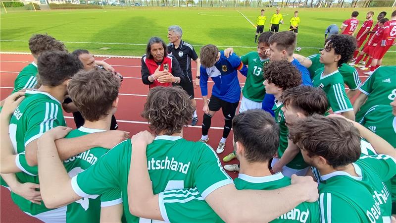 Fußballmannschaft in grünen Trikots mit der Aufschrift 'Deutschland' steht im Kreis auf einer Laufbahn und bespricht sich.