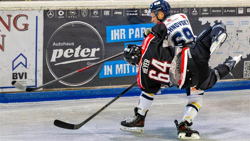 Zwei Eishockeyspieler kämpfen um den Puck, einer trägt schwarze Ausrüstung mit der Nummer 64, der andere weiße Ausrüstung mit der Nummer 69