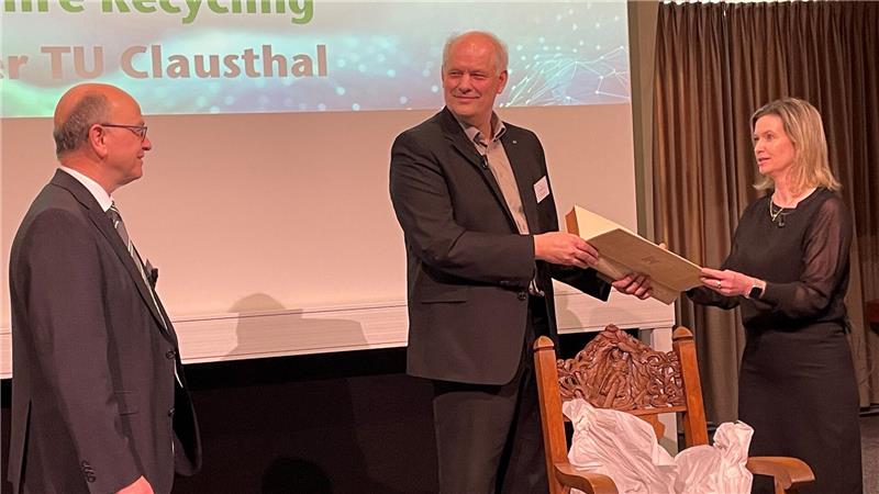 Das Bild zeigt links Professor Daniel Goldmann, rechts Elisabeth Clausen und Bernd Friedrich, die ein Buch in der Hand halten, um es Goldmann als Geschenk zu überreichen.