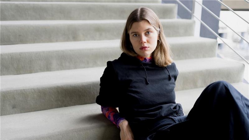 Junge Frau sitzt auf einer Treppe, trägt schwarzen Pullover und dunkle Hose.