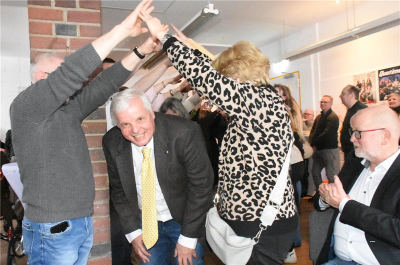 Ein Mann mit Jacket und gelber Krawatte kommt unter einem Spalier durch und lacht.