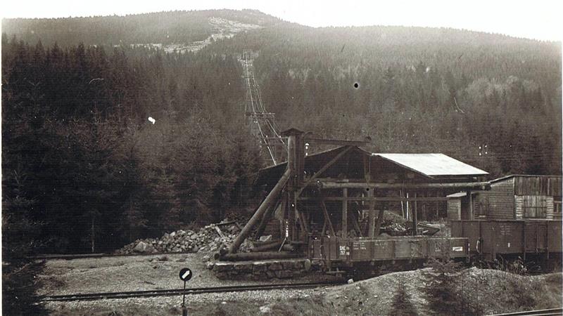 Das alte Schwarz-Weiß-Foto zeigt Güterwaggons und eine Art Seilbahn an einem Berg.