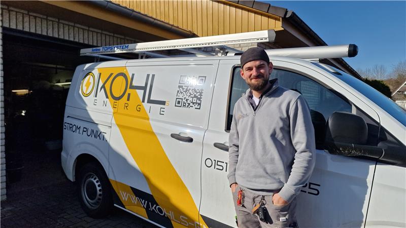 Handwerker steht vor einem weißen Transporter mit gelbem Logo und Schriftzug 'KOHL ENERGIE'