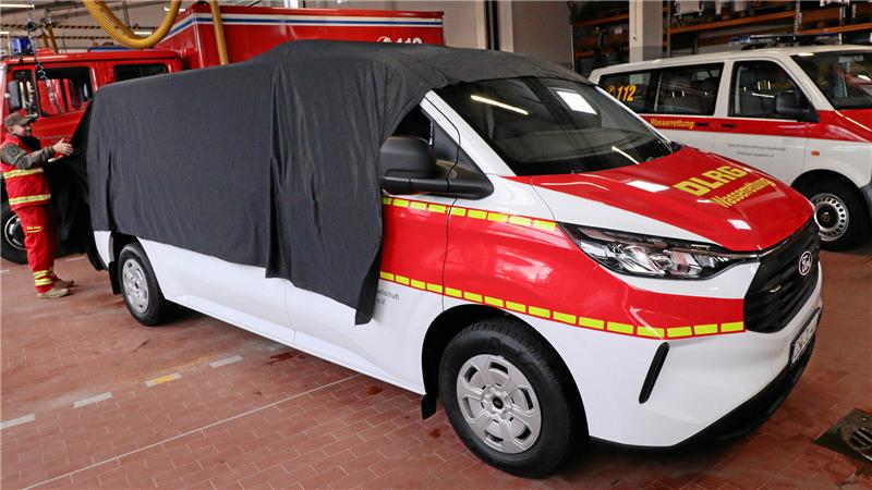 Ein Mann zieht ein schwarzes Tuch von einem Transporter.