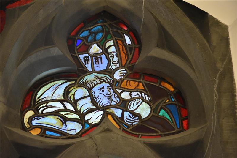 Buntes Kirchenfenster mit zwei bärtigen Männern, einer hält einen Bogen, das Fenster ist dreilappig und von dunklem Stein umrahmt