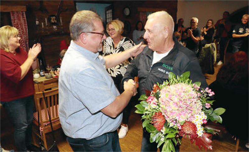 Ein Mann gratuliert einem anderen Mann mit einem Blumenstrauß.