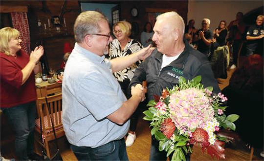 Ein Mann gratuliert einem anderen Mann mit einem Blumenstrauß.