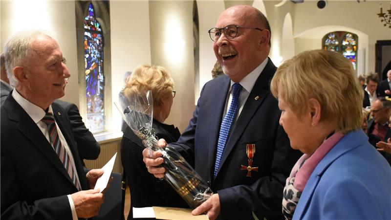 Bundesverdienstorden für den Goslarer Eike Hulsch Ein lachender Mann hält eine Geschenk-Flasche in der Hand und nimmt Umschläge entgegen.