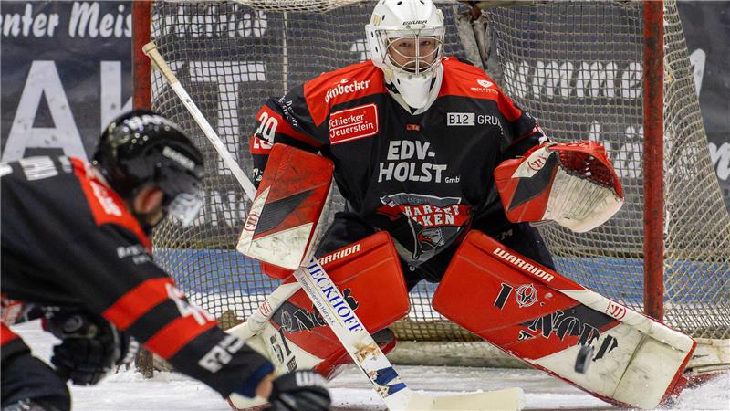 Eishockeytorwart in roter und schwarzer Ausrüstung vor dem Tor in Bereitschaft.