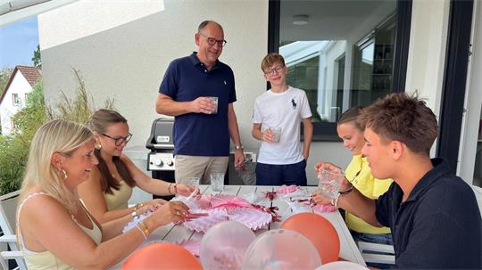Eine Familie sitzt an einem Tisch und bereitet Partyschmuck vor. Vater und Sohn stehen hinter dem Tisch.