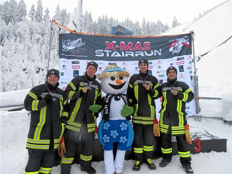Erinnerungsfoto mit Maskottchen: Benedikt Pillach, Lukas Mann, Kevin Diercks und Sven Eisoldt posieren mit ihren Medaillen vor tief verschneiter Schanzen-Kulisse im thüringischen Oberhof. Foto: Feuerwehr Goslar