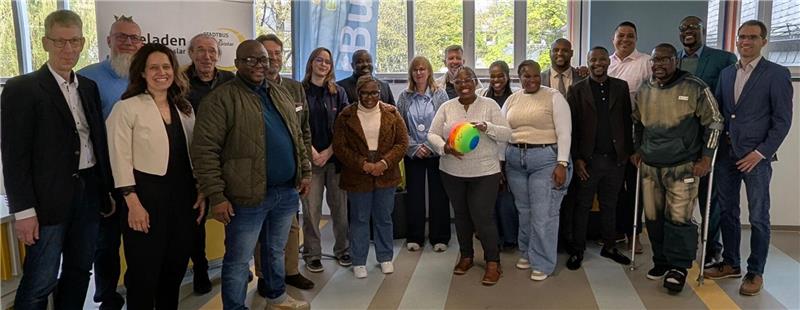 Gruppe von Menschen steht in einem Raum mit großen Fenstern, eine Frau hält einen bunten Ball