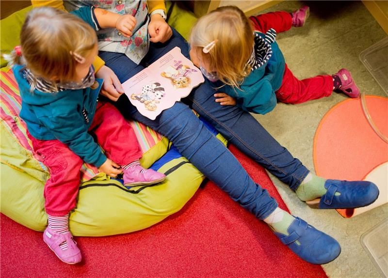 Erzieherin liest mit Zwillingen ein Buch.