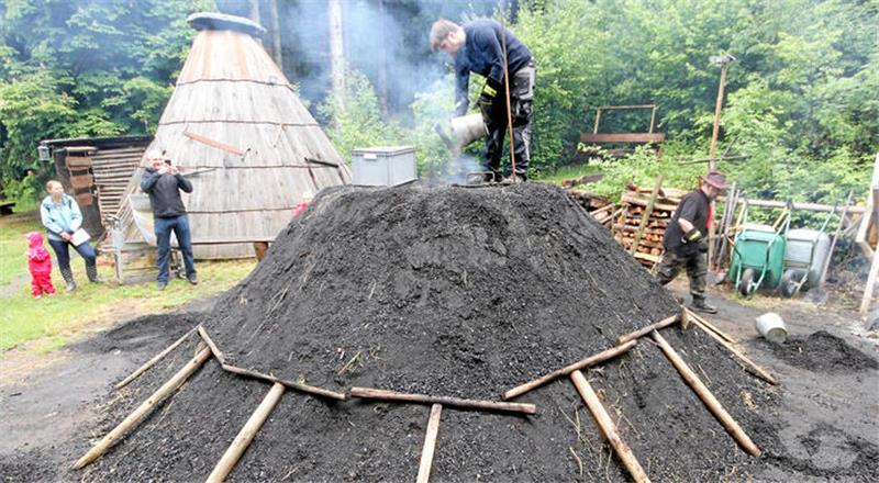 Es geht los: Köhlermeister Simon Wiese kippt die Glut in den Quandel, das ist der Feuerschacht in der Mitte des Meilers.