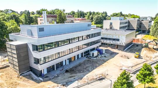 Luftaufnahme eines modernen mehrstöckigen Bürogebäudes mit großen Fenstern und einer Baustelle im Vordergrund.