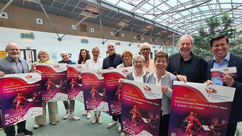 Viele Menschen stehen mit Plakaten in der Hand in einem Raum mit Glasdach und lachen in die Kamera.