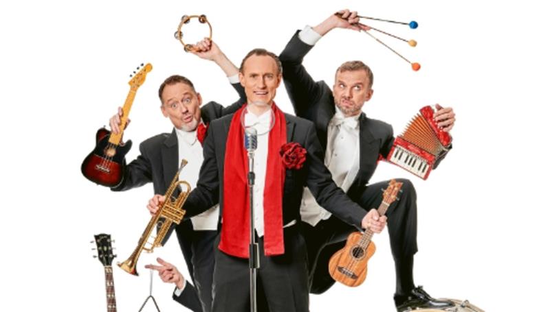 Drei Männer in schwarzen Anzügen mit weißen Hemden und Fliegen posieren mit verschiedenen Musikinstrumenten vor weißem Hintergrund.