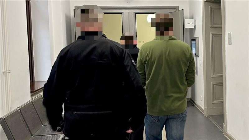 Der 48-Jährige im grünen Pulli wird von zwei Justizbeamten in den Gerichtssaal geführt.